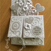 Pop up Silver Wedding Anniversary card made using a number of dies including; Spellbinders nesting plain and scalloped hearts dies, Cheery lynn flowers dies, Anna griffin flourish scroll die, spellbinders lacey circles dies, Crea Nest lies no 33 dies, leabilities frame square curve die set (for small flourishes). Joy cut & emboss wedding die set, Nellies nesting stitched squares dies, Background embossed with distress ink applied to folder using embossaliscious a4 folder. die cuts inked whilst in die in matching distress ink (Hickory Smoke). - craftybabscreativecrafts.co.uk