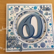 60th Birthday Spinner card made using various dies including; 660223 Sizzix Thinlits Die Set 13PK - Celebration Words Script by Tim Holtz, 662228 Sizzix Thinlits Die Set 69PK - Script, Upper & Lower Case dies by Tim Holtz, 656617 Sizzix Bigz Sassy Serif Numbers dies, Tattered lace Essentials nesting circles dies and Crealies DOUBLE STITCH Die Set No.33 CIRCLE Cutting Dies XXL33 , Numbers, words and letters cut from 2 shades of blue card and heat embossed with clear embossing powder Background inked through stencil with various shades of Blue Tim Holtz distress inks, 'Fabulous' Sentiment stamped using FOREVER-FRIENDS-OPULENT-A5-Clear-Stamp-Set-Docrafts. Highlights and accents added using Spectrum Noir Sparkle clear overlay pen. - craftybabscreativecrafts.co.uk
