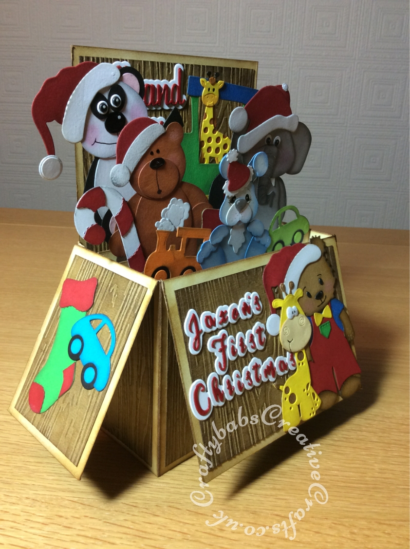 XL sized Toy Box POp Up Baby's First Christmas Card made using various dies including, Toffee bear standing die by Tinker & Co, Jessie bear and outfits dies, Sizzix originals Train, Stocking and Candy cane dies, Spellbinders Die D-Lites Little Guy dies, Bosscut bunnies die, unbranded giraffe dies, Craftycat cistom wooden bear die, Quickutz revolution build an animal dies. Paper boutique sentiment dies and Gemini Expressions Metal Die - Uppercase and lower case Alphabet Sets. - craftybabscreativecrafts.co.uk