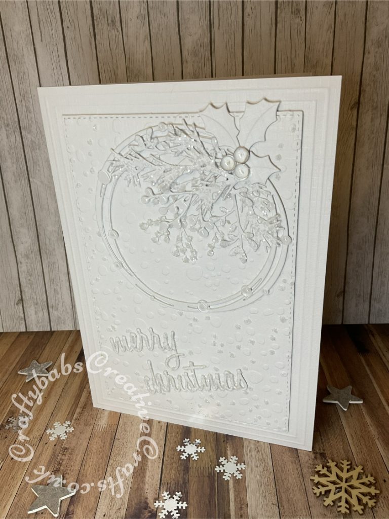 White on white Christmas card inspired by a card on Pinterest https://www.pinterest.co.uk/pin/555983516510989238/ Made using various dies including:- Starlight Circle Die Set, Skip to the beginning of the images gallery Sizzix Thinlits Die Set 17PK - Holiday Words: Script, Sizzix - Tim Holtz - Alterations Collection - Thinlits Dies - Holiday Greens, Marianne holly die and Crafters companion textures embossing folder - rain. - craftybabscreativecrafts.co.uk